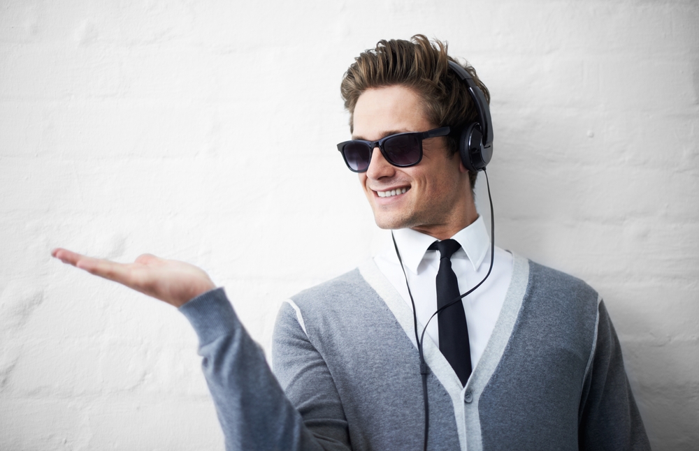 A trendy young man holding out his palm while listening to music on his headphones.