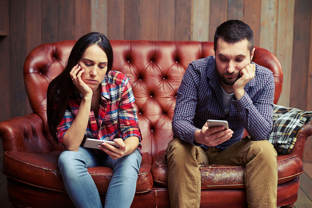 bored young couple sitting on couch and looking at their phone screens