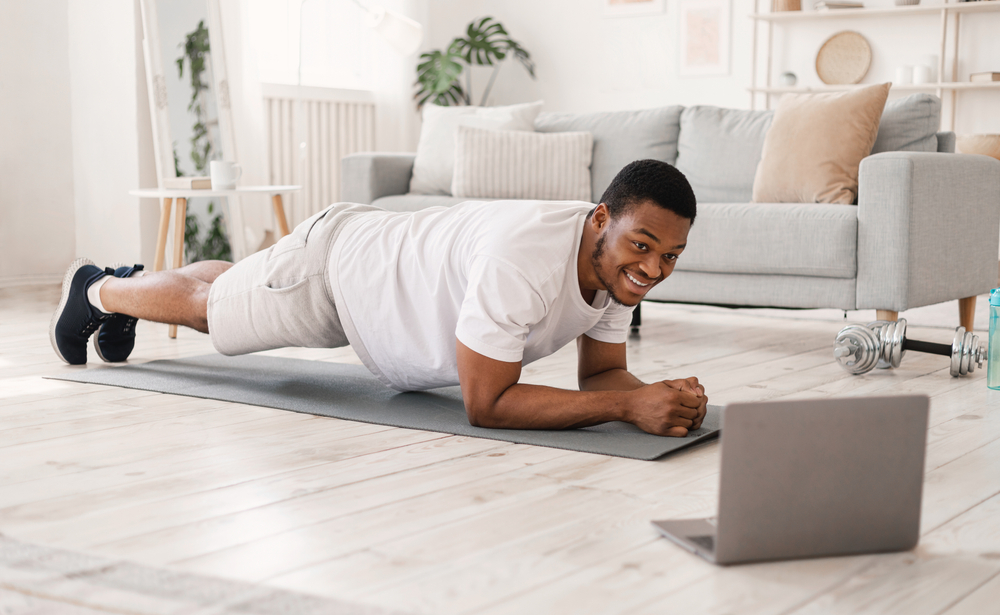 Man Exercising Doing Plank Exercise At Laptop During Online Workout Indoors